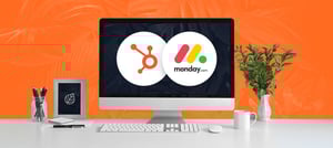 Imagem de uma mesa de trabalho com um computador. Na tela do computador há o logo a plataforma HubSpot e do CRM Monday, representando a integração entre as duas plataformas para desenvolvimento de projetos personalizados - Tropical Hub