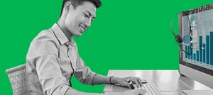 homem em frente ao computador sorrindo e anotando num bloco de papel